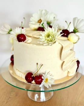 A buttercream layer cake topped with fresh cherries and daisies