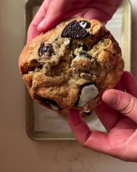 A hand holding a thick bakery-style chocolate chip cookie