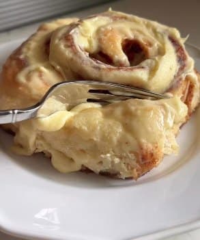 A cinnamon roll covered in cream cheese icing, pulled apart with a fork